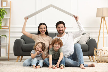 Family housing concept. Happy woman and her husband holding plastic roof while sitting with kids on...