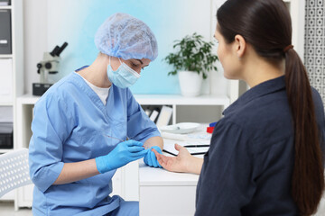Fototapeta premium Laboratory testing. Doctor taking blood sample from patient at white table in hospital