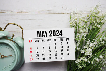 May 2024 monthly calendar and alarm clock on wooden background