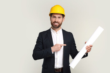 Architect in hard hat pointing at draft on gray background