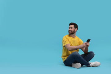Smiling man with smartphone on light blue background. Space for text