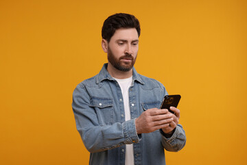 Handsome man with smartphone on orange background