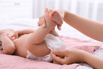Mom changing baby's diaper on bed at home, closeup