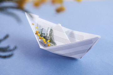 Spring is the time of dreams: a paper boat from a music book with mimosa branches, close-up