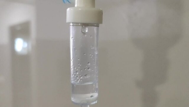 Intravenous IV drug infusion drip medicine liquid drops (sodium, glucose or saline solution) falling inside plastic tube. Dripping equipment closeup side view. Healthcare healing and recovery concept.