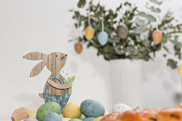 Wooden easter bunny and colorful eggs on a eucalyptus plant in a vase, on table at home