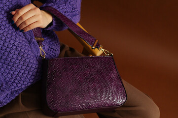 Autumn, winter fashion details. Close up photo of trendy purple  faux leather woven bag, purse in elegant outfit. Woman posing on brown background. Copy, empty, blank space for text - 765090730