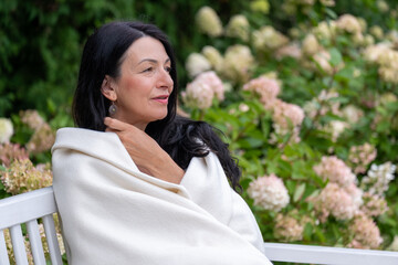 A mature woman, wrapped warmly, gazes into the distance, her expression one of peaceful...