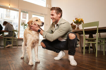 Close up portrait of happy dog owner, man with his pet giving a treat, spending time in animal-friendly cafe or co-working space