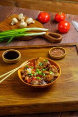 Thai chicken with rice and vegetables in a plate on a wooden table next to soy sauce sticks and vegetables in the background