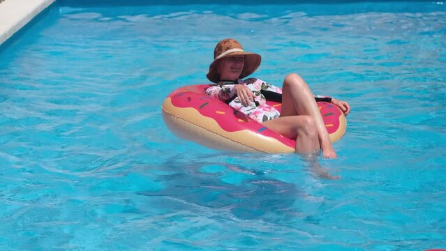 Woman on inflatable lap with beach ball in swimming pool sunny day. Funny summer vacation