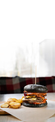 Craft big black beef burger and french fries on wooden table on blurred background.