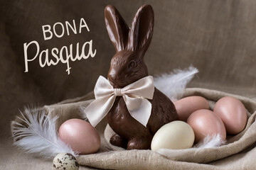 Happy easter text in catalan with bunny with bow and chocolate easter eggs. - obrazy, fototapety, plakaty