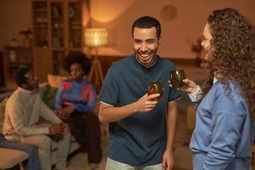 Waist up portrait of young man laughing joyfully enjoying drinks and conversation during house...