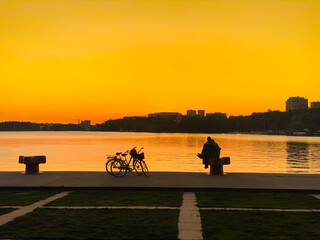 Beautiful spring city sunset with two people sitting by waters edge with orange sky.