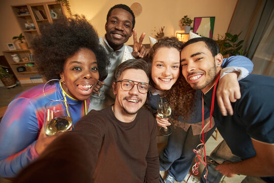High angle portrait of cheerful adult friends huddling together and taking selfie photo at home smiling at camera
