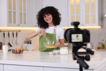 Smiling food blogger cooking while recording video in kitchen