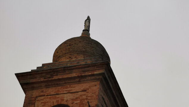 Campanile di una chiesa visto dal basso che si staglia nel cielo grigio autunnale
