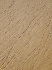 Wet sand background with intricate patterns, captured on the Atlantic coast of Portugal, highlighting the unique textures shaped by ocean waves.