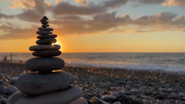 4K video. Copyspace. Pyramid of little stones on pebble beach. Setting sun, sunset, waves, coast. Sea shore zen. Concept of calm, yoga, self-improvement, construction, travel, tourism, rest, relax