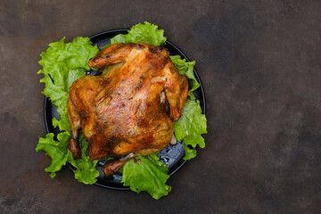 Chicken grill on lettuce on leaves on black plate isolated on dark brown background. Top view.