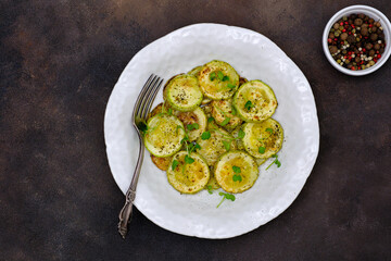 Fried zucchini with lemon zest and thyme on dark brown background. Top view.