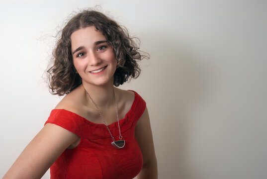 young brunette curly hair woman smiling and wearing red dress white background