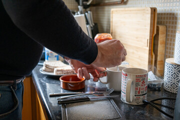 Male in the kitchen making tea and cutting sausage with knife and fork. 