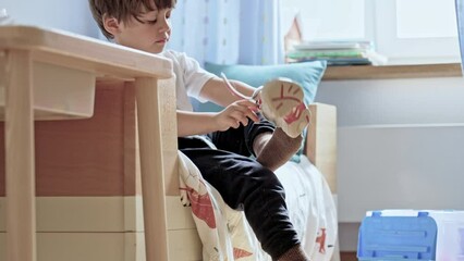 Self-Sufficiency In Action - Young Boy Fastens Velcro Sneakers And Dashes Away. Child Sitting By The Side Of Bed Clothing Himself During Morning Routine - Powered by Adobe