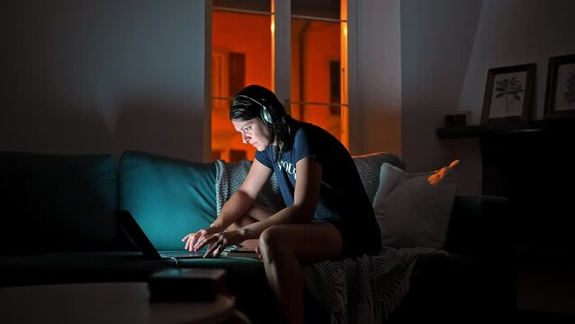 Woman Browsing Internet In Living Room At Night Sitting On Couch. Anxious Person In Front Of Modern Device In The Evening