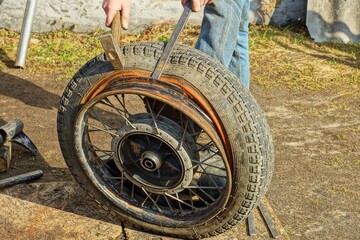 a worker in brown mittens uses tools to remove an old black rubber tire from a rusty iron rim from...