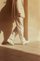 Art style: Modern, minimalist fashion photography of a person wearing a beige suit and white sneakers, walking in an urban setting