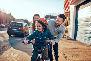 Happy family teaching child to ride a bicycle outdoors