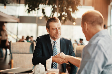 Businessmen shaking hands at an indoor cafe after making a deal