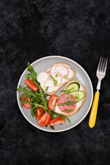 Different tapsas sandwiches with vegetables, radish, sausage, tomatoes, arugula on grey plate on dark background. top view.