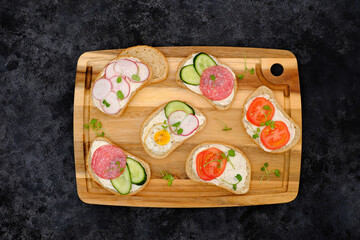 Different tapsas sandwiches with vegetables on cutboard on dark background. top view.