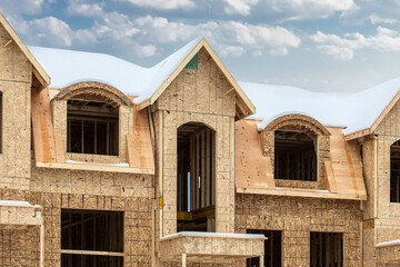Exterior walls with window and door openings sheathed in plywood at a residential construction site in winter with snow on the roof.