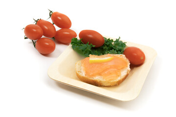 smoked salmon on a slice pr crusty bread with grape tomatoes on a sustainable bamboo plate isolated on white