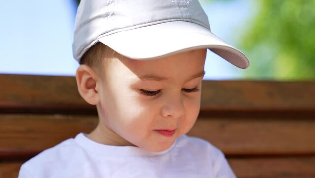 Cropped image of a little Caucasian kid wearing a cap. Cute baby boy looking down and waving hand. Close up.