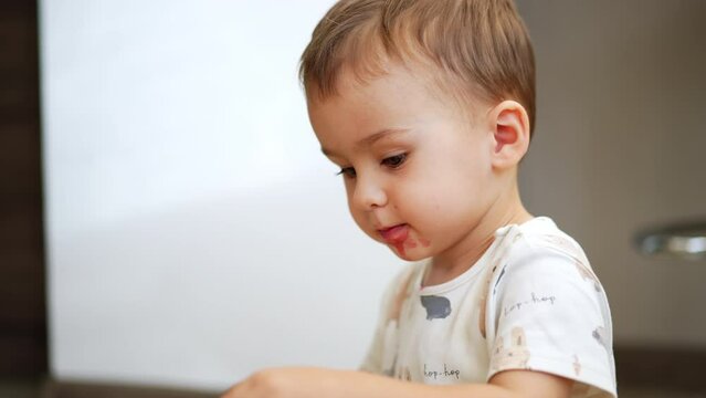 Beautiful smiling Caucasian toddler with smudged face. Toddler takes the raspberries from mom's palm. Close up.