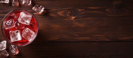 A glass of red beverage with ice on a wooden surface