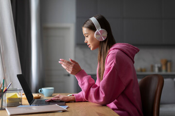 Teen schoolgirl in headphones studying online with remote tutor from home, student using laptop...