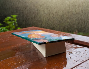 Painted half-close-up painting resting on brown table in the rain  - 765195591