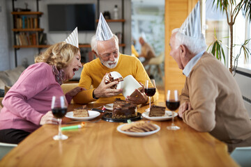 Happy senior man receiving a Birthday present from his friends  at home.
