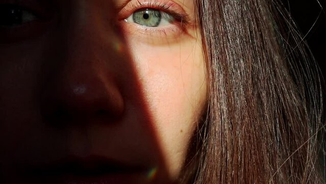 Beautiful girl with blue eyes looking into a camera. Woman's face with colorful highlights, sparkles FullHD footage. Sunny bunnies. Dark portrait.