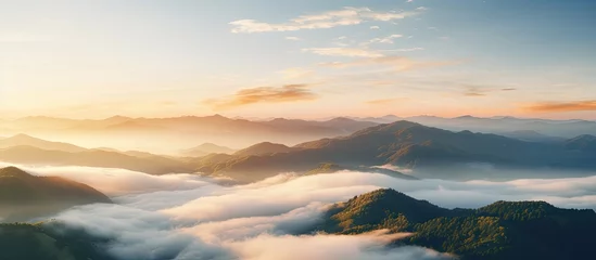 Fotobehang A breathtaking aerial view of a mountain range engulfed in clouds at sunset, with the suns warm light creating a stunning afterglow in the atmosphere © TheWaterMeloonProjec