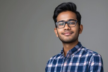 Studio shot of young Indian businessman wearing checkered shirt against gray background