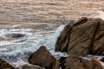 Beach waves at sunrise sunset over rocks on the coastline beach