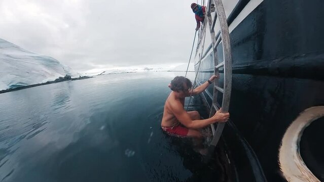 Man swims in Antarctica. Young man jumps into the icy water from the boat anchored near the Antarctica