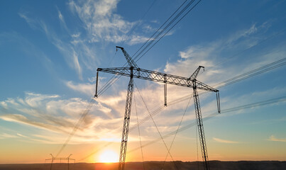 Dark silhouette of high voltage tower with electric power lines at sunrise. Transmission of...